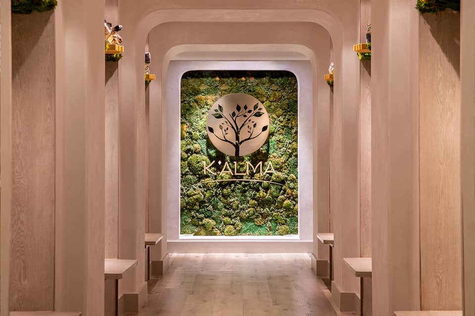 Modern spa entrance with moss wall and KALMA logo under rounded archway with wooden paneling