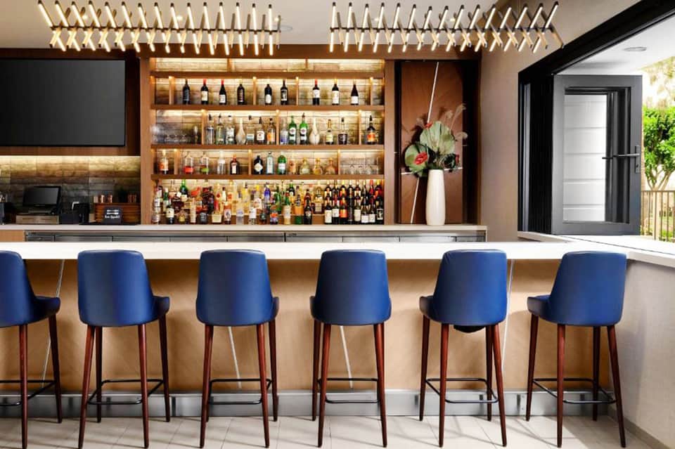 Contemporary bar with blue bar stools, illuminated shelving displaying spirits, and elegant gold pendant lighting