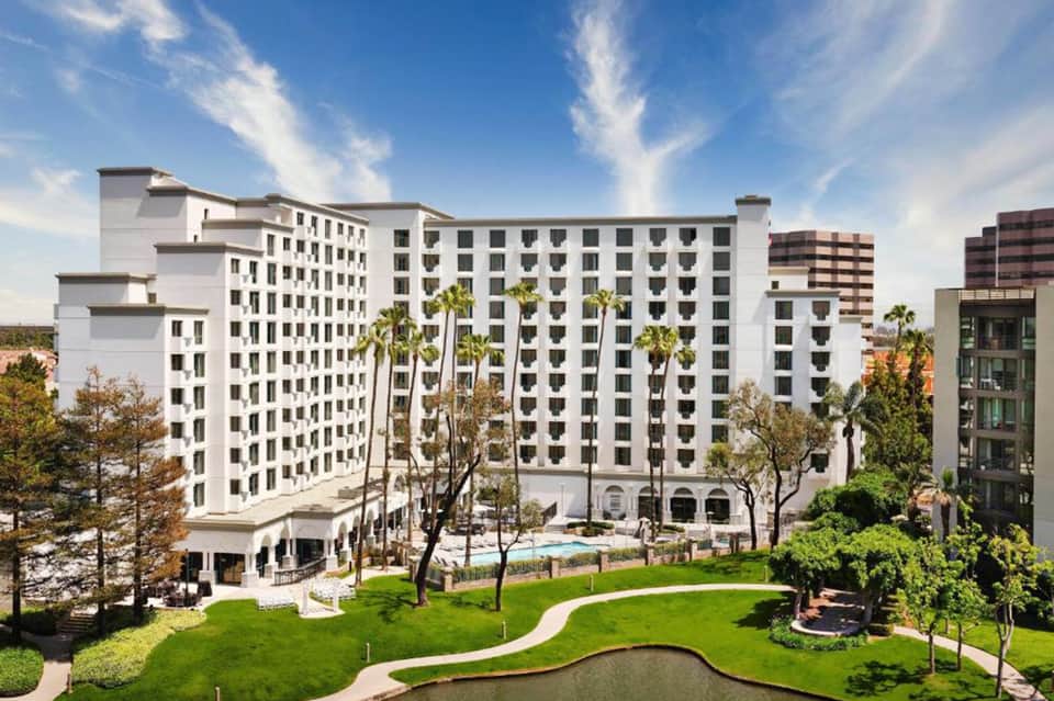 Modern white hotel building with palm trees and manicured lawns surrounding an outdoor pool area