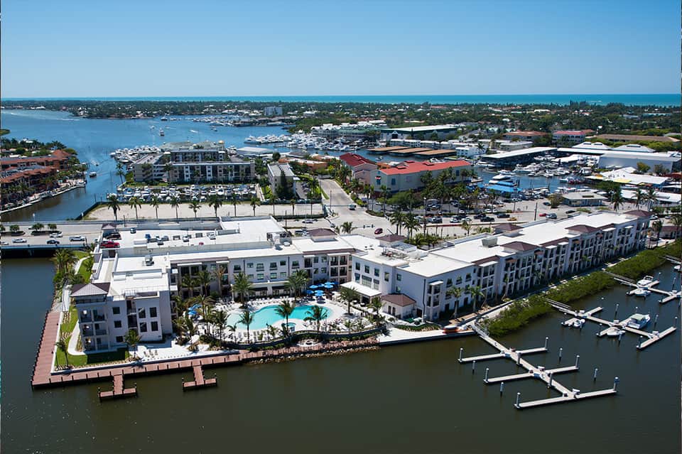 Aerial view of modern waterfront resort with white buildings, pool, and marina with boats