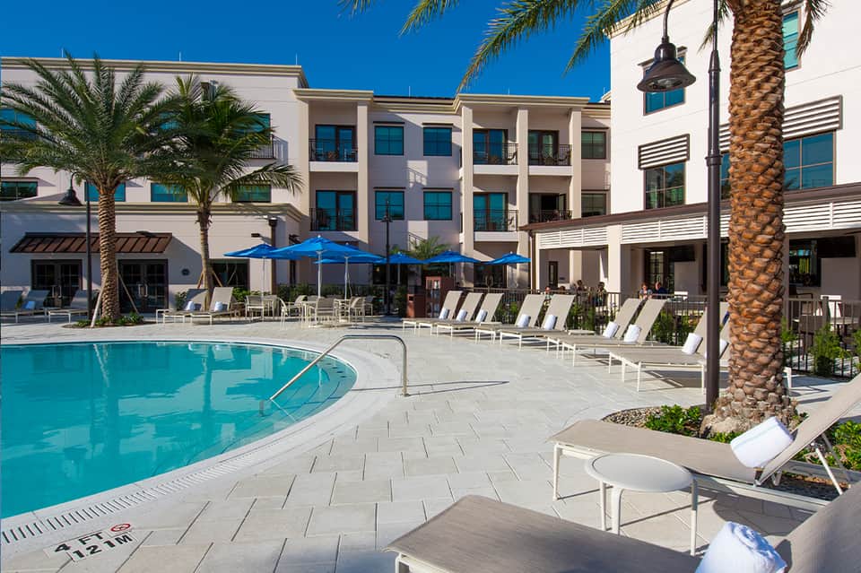 Resort pool courtyard with blue umbrellas, palm trees, white lounge chairs, modern architecture