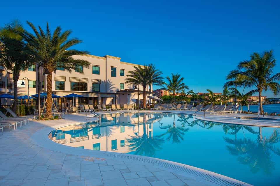 Resort pool with reflection of palm trees, lounge chairs, and waterfront building