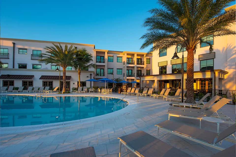 Curved resort pool at golden hour with palm trees, loungers, and Mediterranean-style buildings