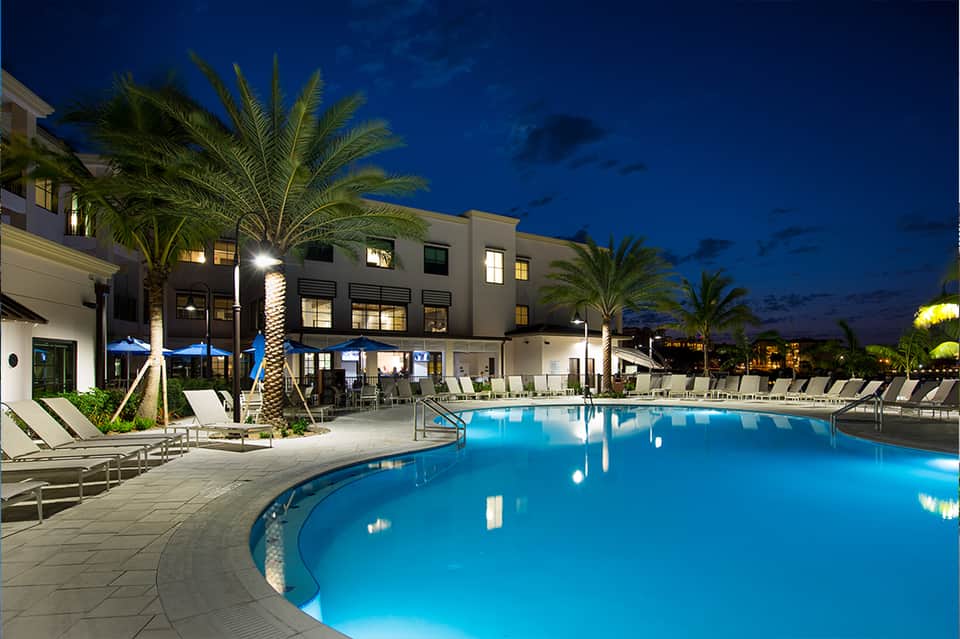 Resort swimming pool at twilight with palm trees, lounge chairs, and illuminated hotel building