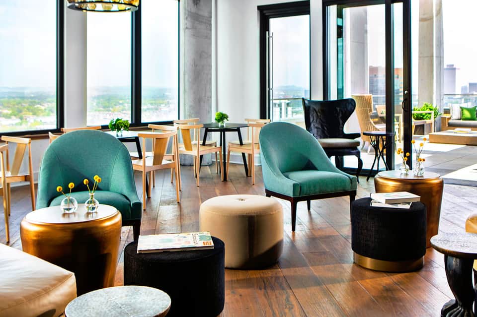 Upscale lounge with teal chairs, gold side tables, wooden flooring, and panoramic city views