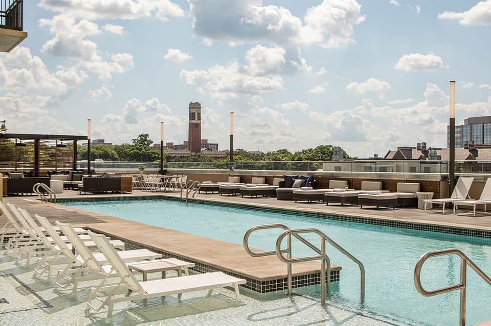 Rooftop pool deck with lounge chairs, umbrellas, and city skyline views including historic tower