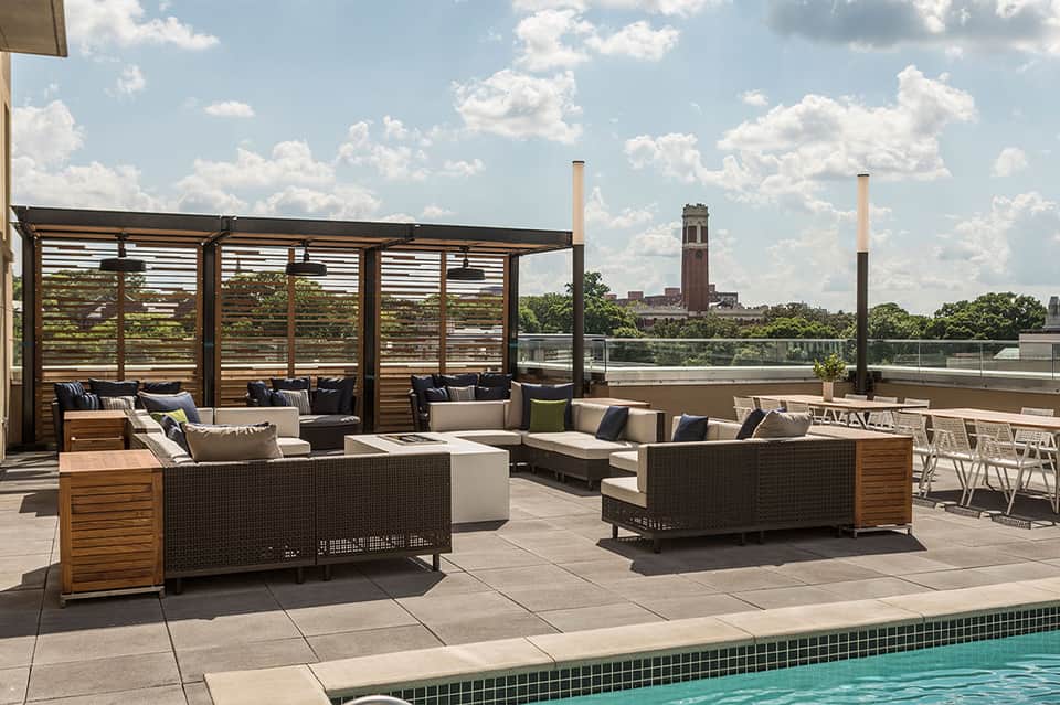 Rooftop terrace with woven lounge seating, wooden pergolas, and city skyline view in background