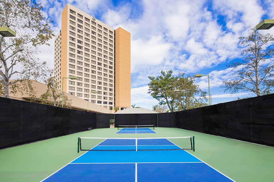 Tennis courts with blue and green surfaces surrounded by black netting near tall residential building