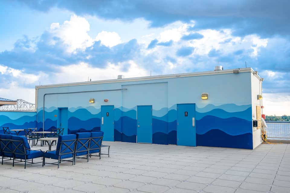 Waterfront restroom facility with blue wave mural design and outdoor seating area