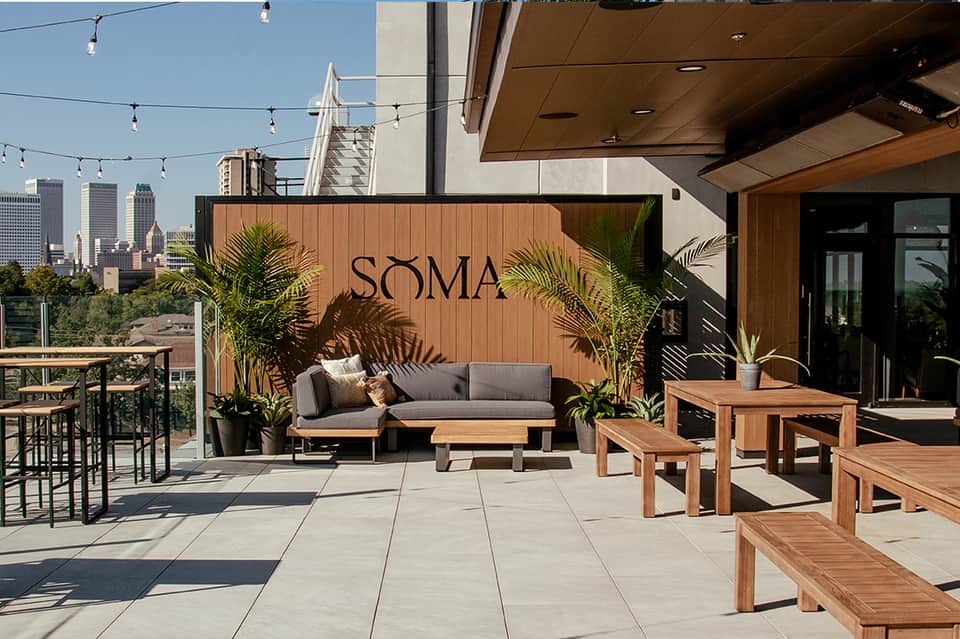 Modern rooftop terrace with SOMA signage, wooden furniture, and city skyline views