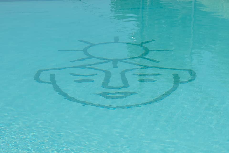 Swimming pool with artistic sun face design visible underwater on pool floor
