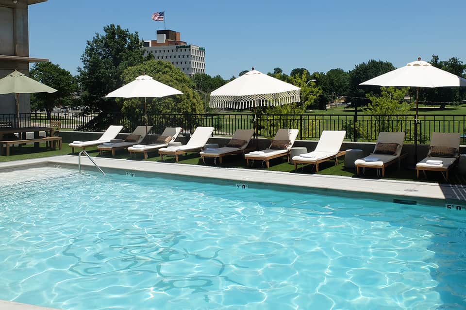 Rectangular pool with white umbrellas and lounge chairs on manicured lawn near downtown