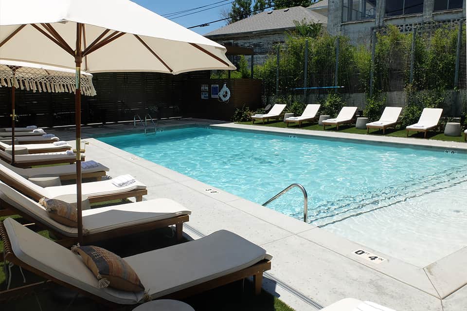Resort pool with crystal blue water, lounge chairs with umbrellas, and manicured landscaping