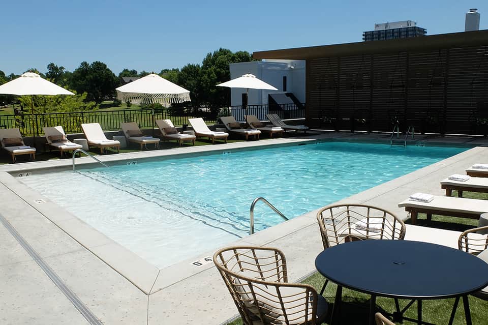 Resort pool deck with lounge chairs, white umbrellas, and manicured grounds under clear sky