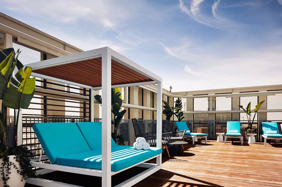 Modern rooftop deck with white pergola, turquoise loungers, wooden decking, and city views