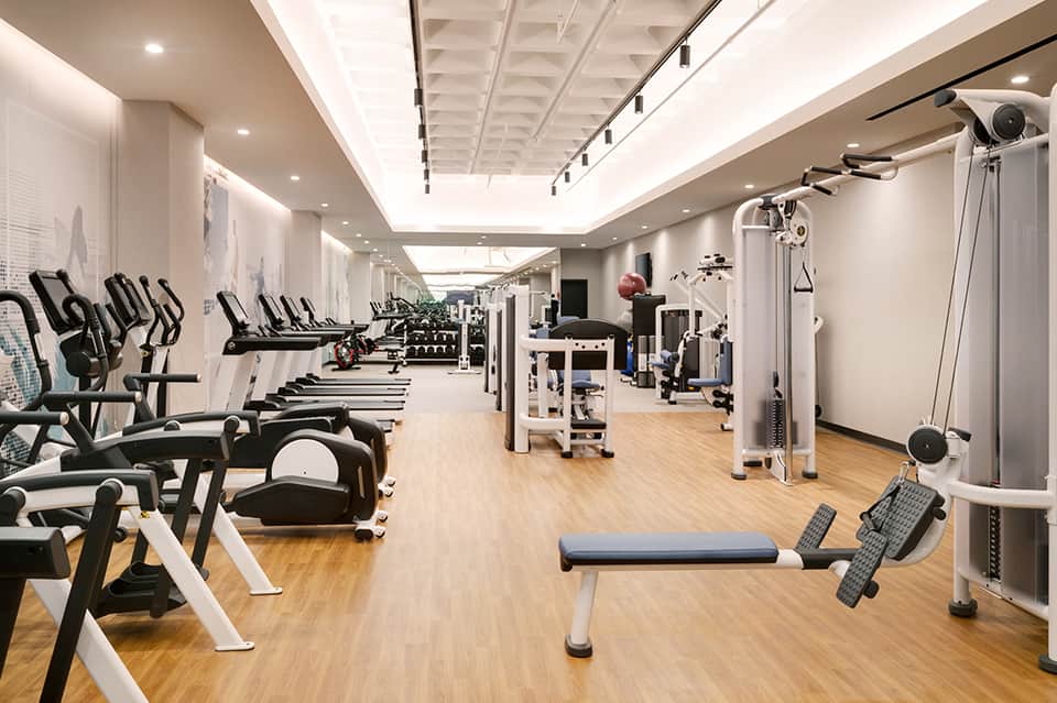 Modern gym interior with cardio machines, weights, and equipment on wooden flooring