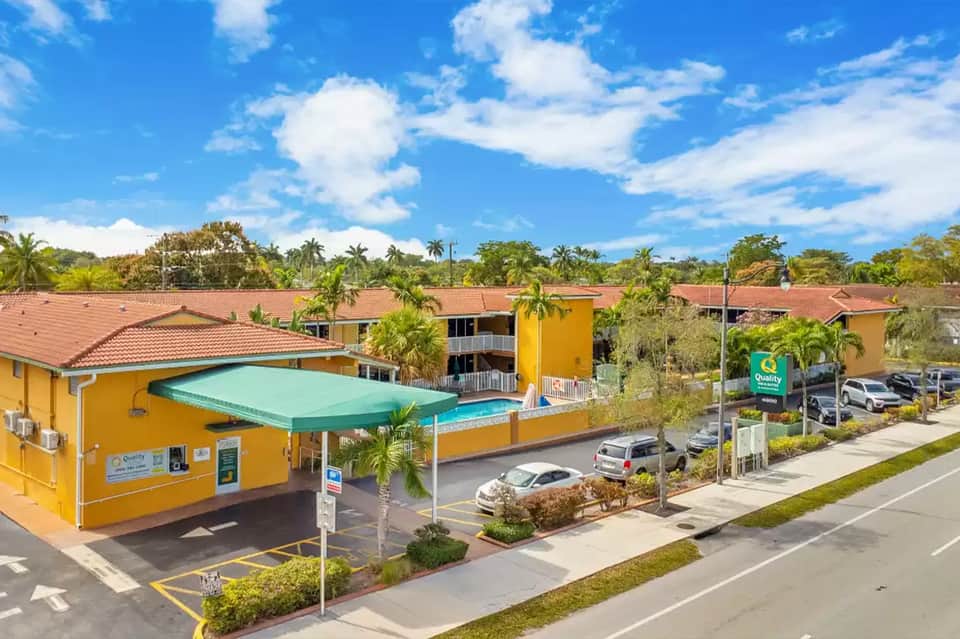 Aerial view of yellow Quality Inn motel with turquoise pool canopy and parking lot