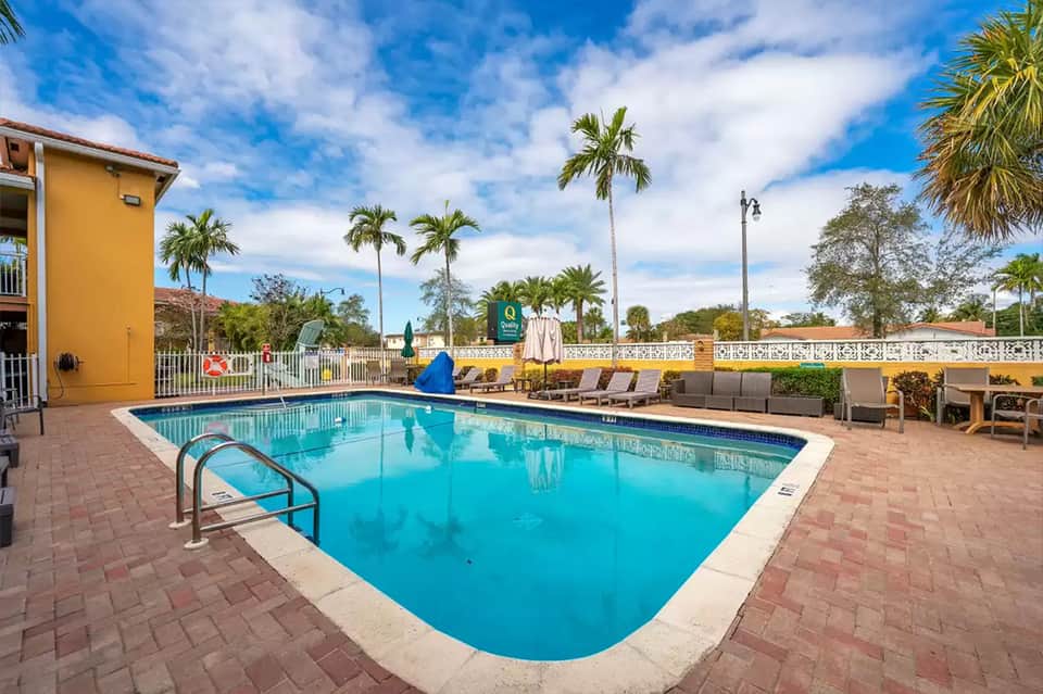 Bright blue swimming pool surrounded by lounge chairs and palm trees at sunny resort
