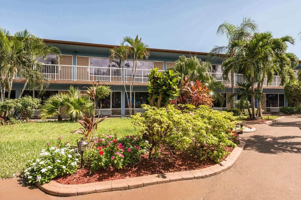 Two-story resort building with tropical landscaping, palm trees, and colorful flower gardens in courtyard