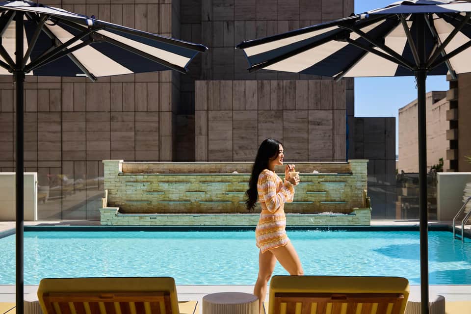 Woman in patterned dress walking by outdoor pool with lounge chairs and umbrellas