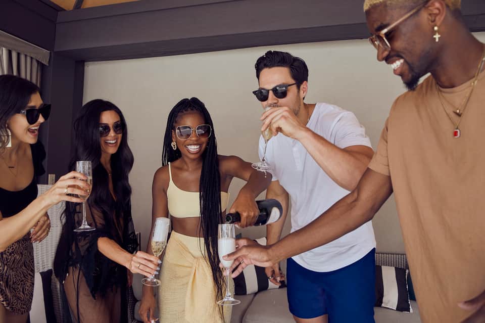 Group of five people toasting with champagne glasses at an indoor celebration or party