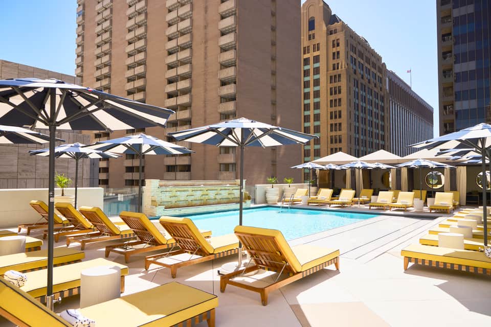 Urban rooftop pool with yellow lounge chairs, black umbrellas, and downtown skyline backdrop