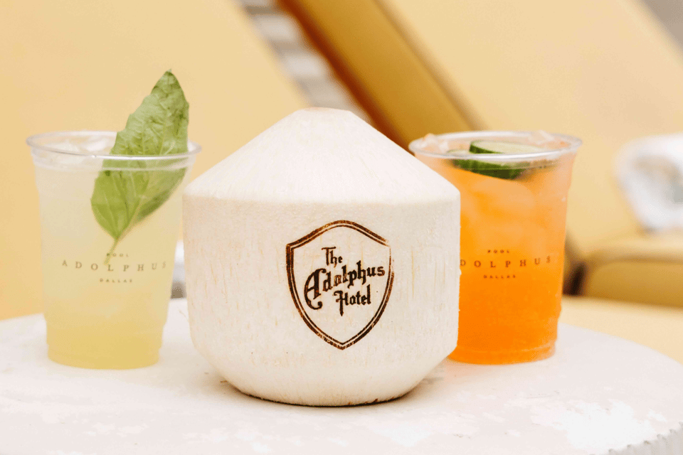 The Adolphus Hotel branded white coconut drink with two colorful cocktails on either side