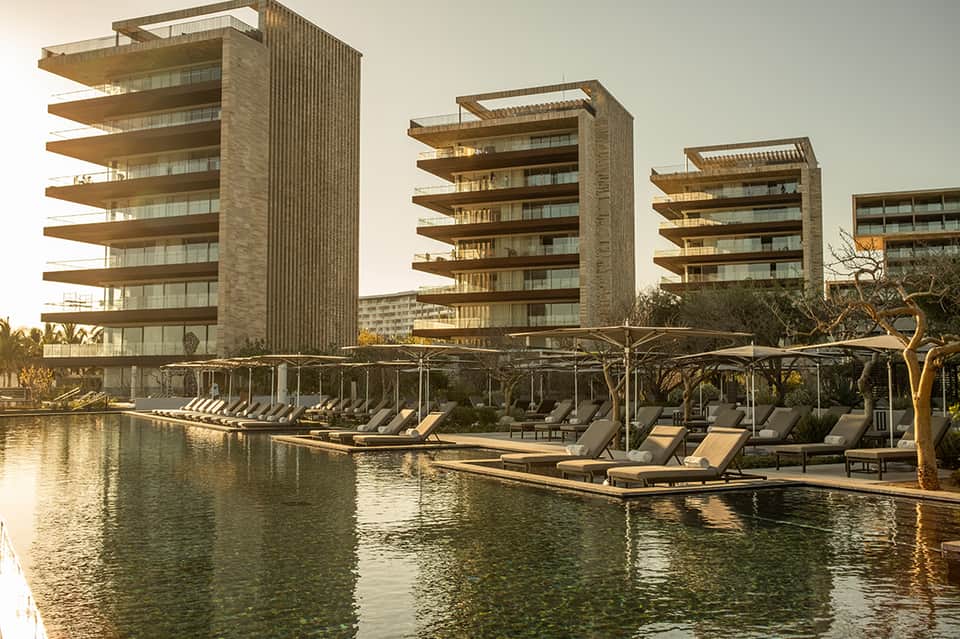 Multi-story residential towers reflected in waterfront with lounge chairs on dock and landscaping