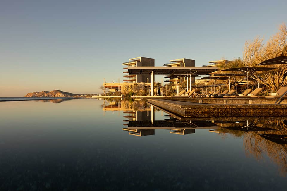 Modern spa building reflected in still water at golden hour with island landscape in background