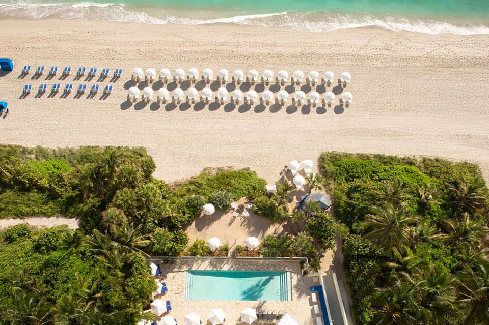 Aerial view of pristine beach with organized rows of white umbrellas, turquoise water, and tropical vegetation