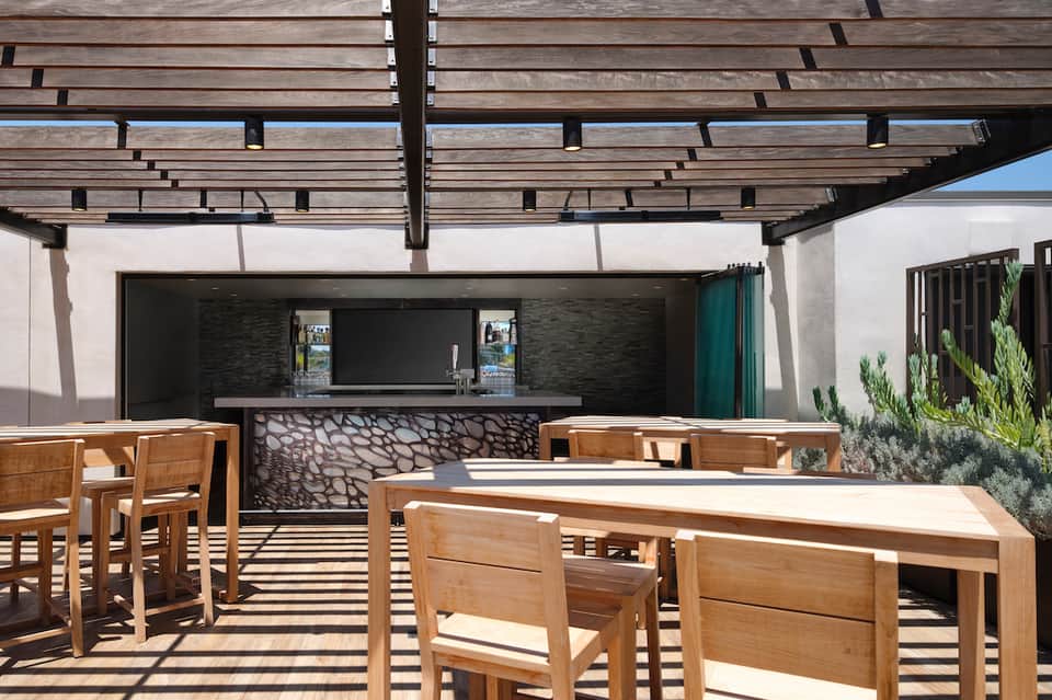 Modern outdoor bar and lounge area with wooden pergola and stone counter seating