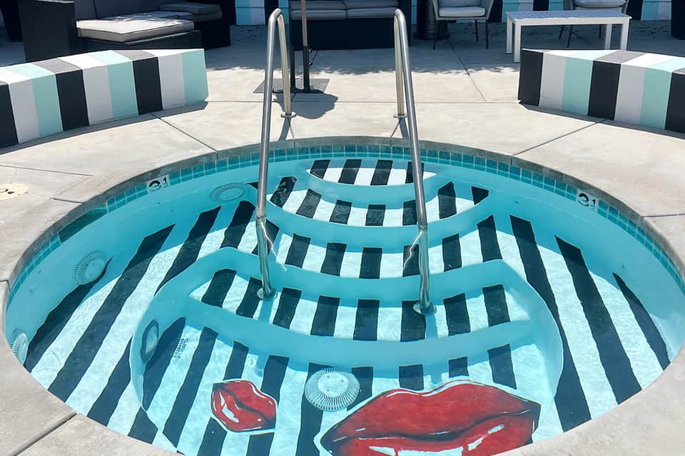 Empty drained pool with blue walls, black and white striped pattern, and artistic red lips design