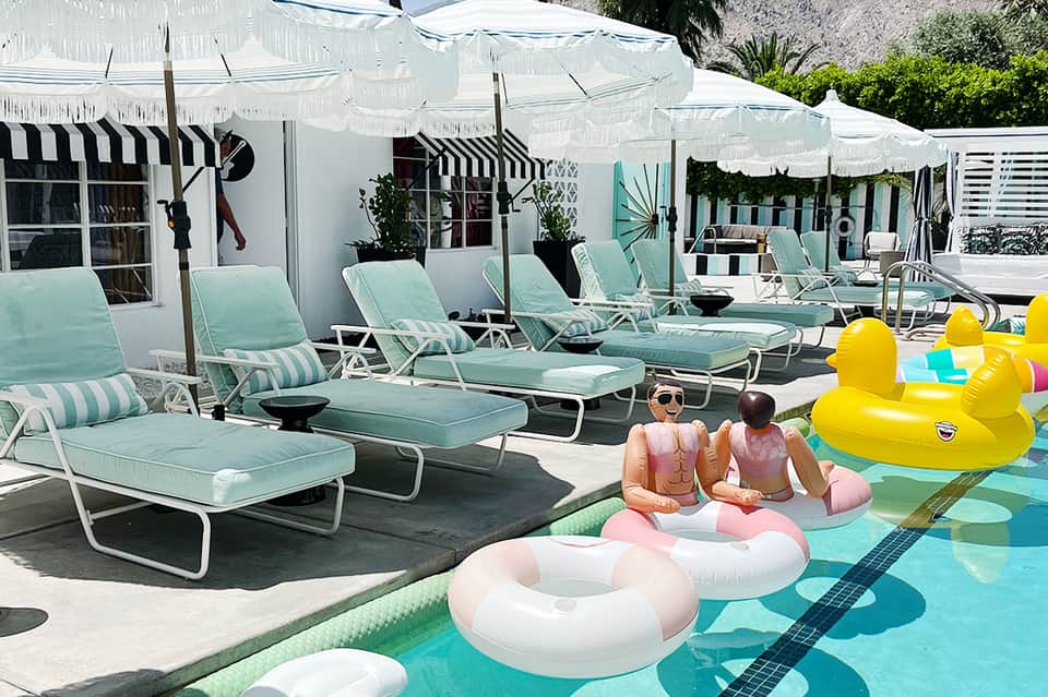 Resort pool deck with turquoise lounge chairs, white umbrellas, and guests on colorful pool floats