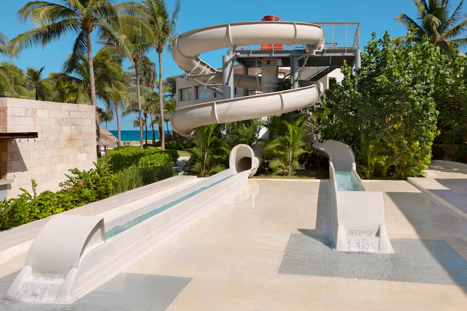 White spiral water slides descending from multi-level structure surrounded by palm trees and tropical landscaping