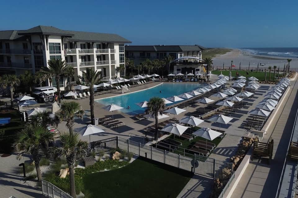 Beachfront resort pool with white umbrellas, palm trees, and ocean view with sandy beach in background