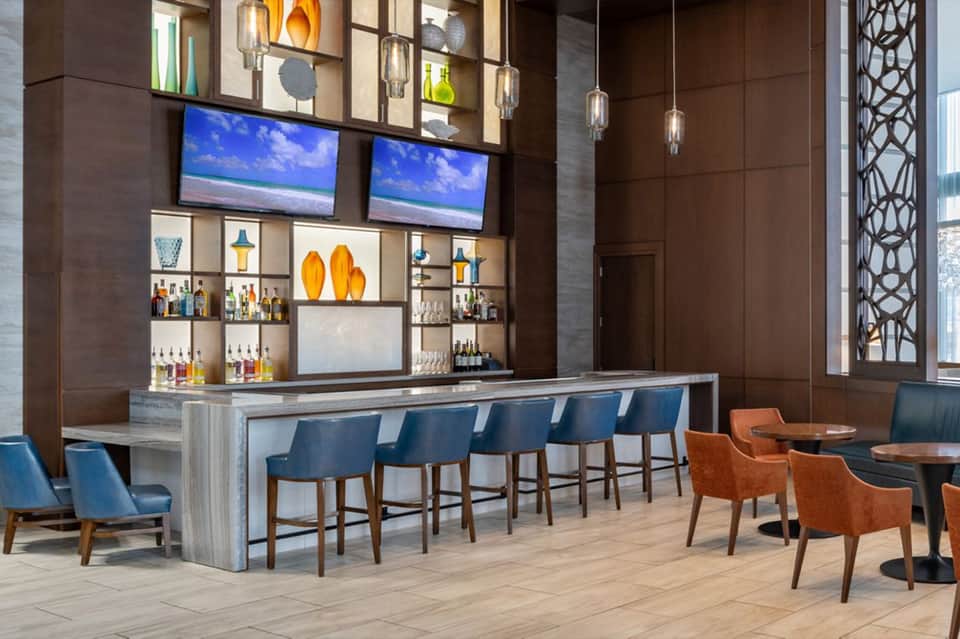 Modern hotel bar with blue seating, wooden countertop, and shelving displaying spirits