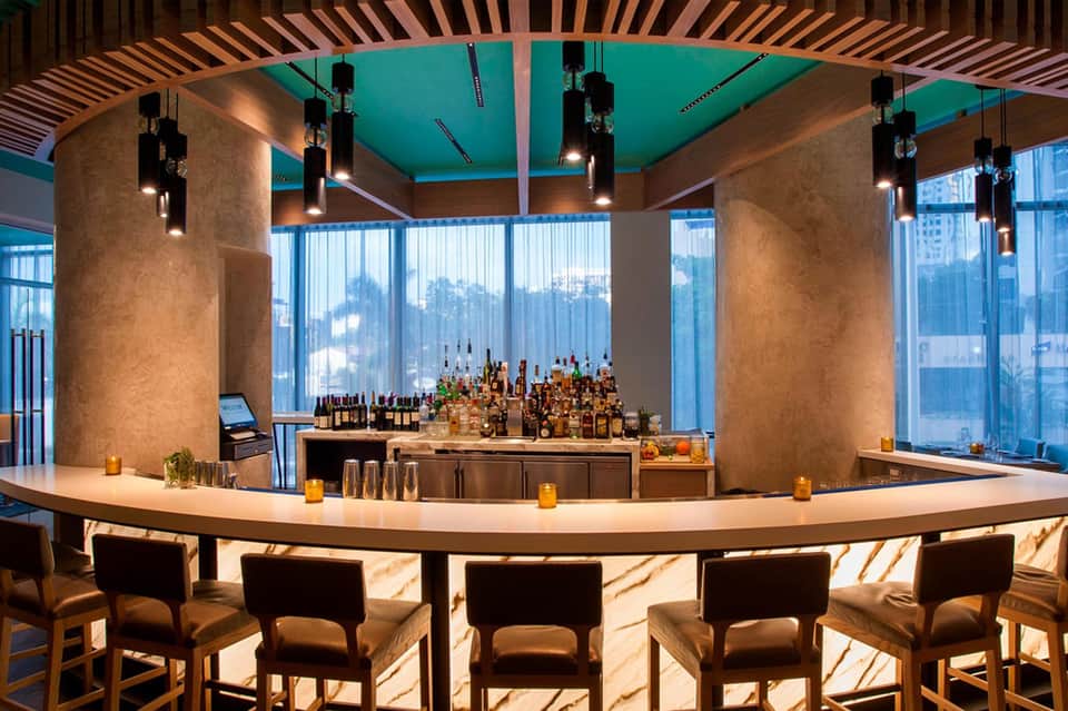 Modern curved bar with turquoise ceiling, pendant lights, and floor-to-ceiling windows