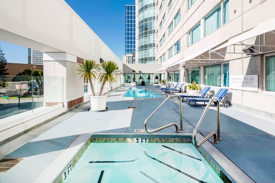 Modern hotel rooftop pool deck with lap pool, loungers, and city skyline views