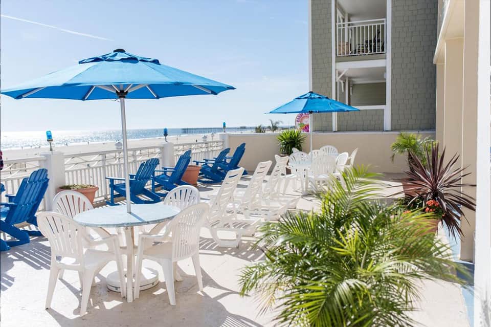 Beachfront deck with white Adirondack chairs, blue umbrellas, and ocean view at resort