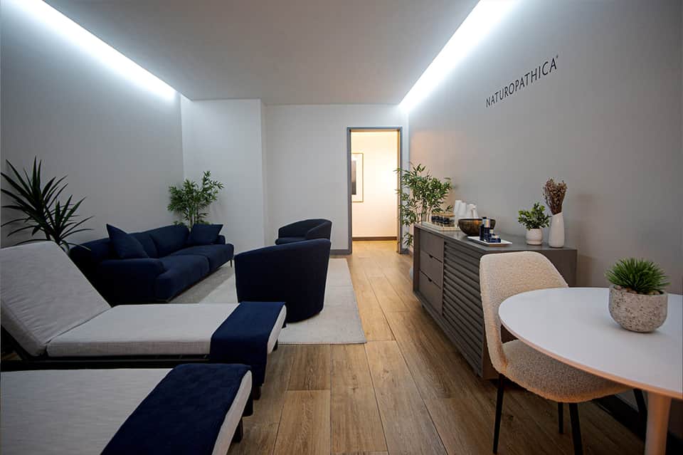 Contemporary spa lounge with navy blue seating, potted plants, wooden flooring, and Naturopathica branding
