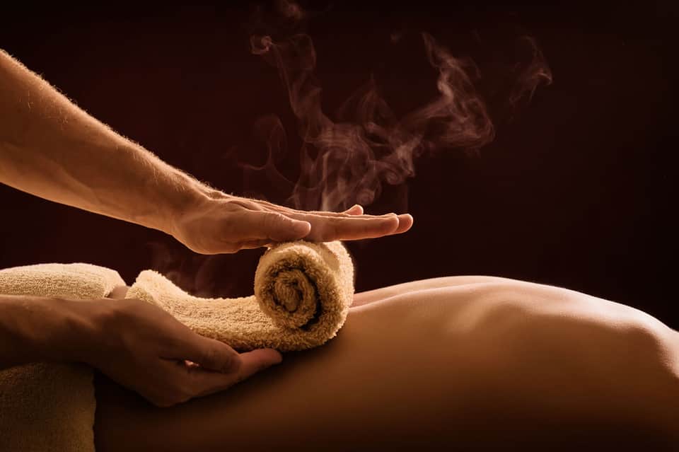 Spa therapist applying hot towel treatment to client's back during wellness massage
