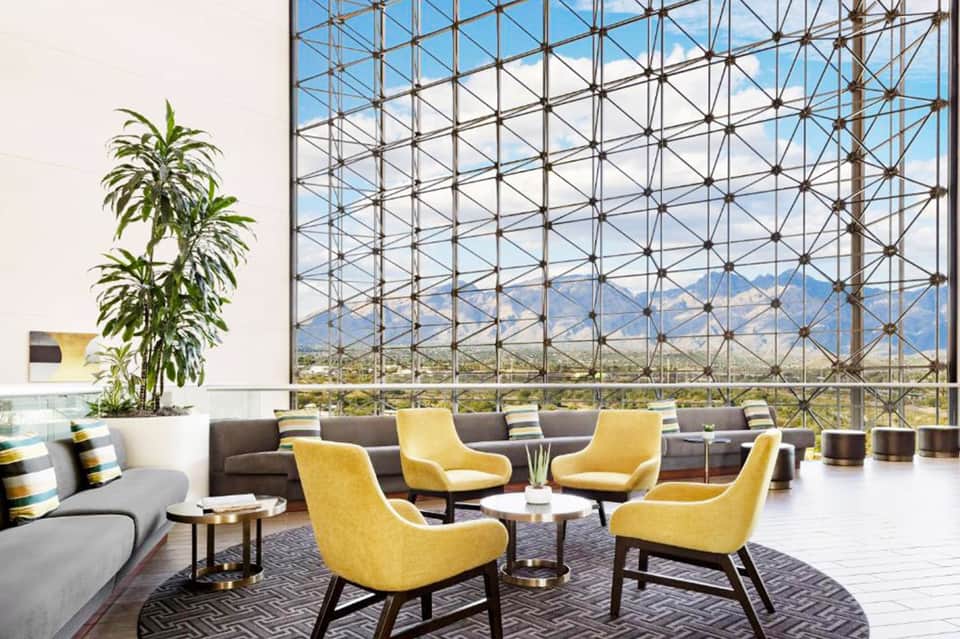 Modern lounge with yellow chairs, gray sofa, and floor-to-ceiling windows overlooking mountains