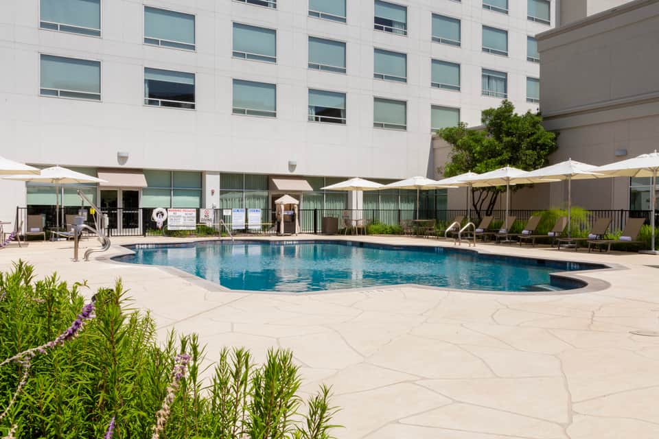 Modern hotel pool with white umbrellas, lounge chairs, and multi-story building with grid windows