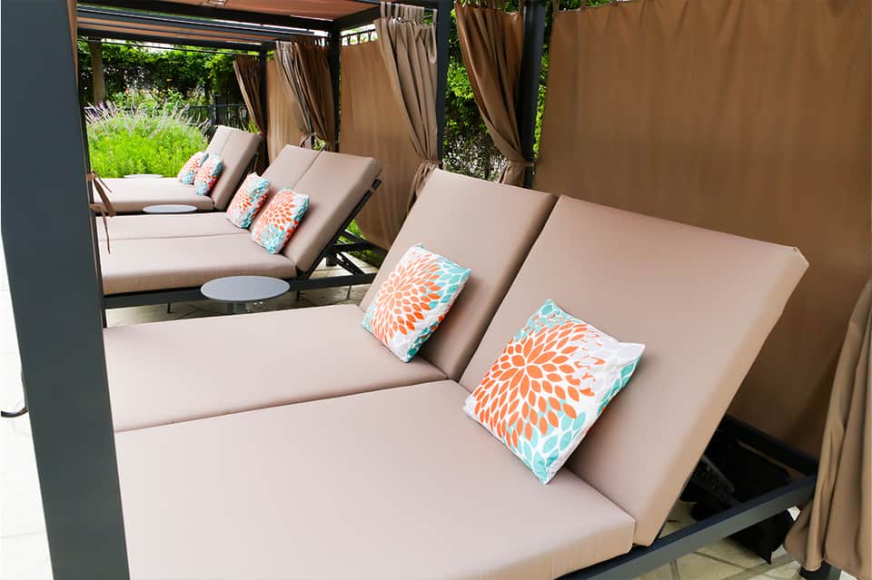 Luxury outdoor cabanas with beige cushions, colorful pillows, and tan curtains surrounding a pool area