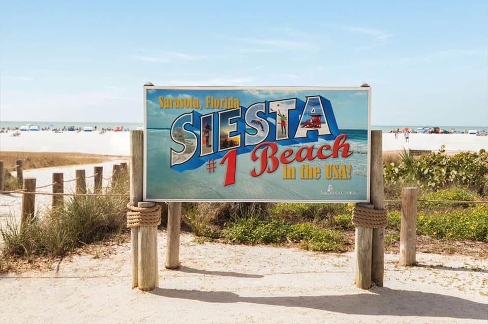 Siesta Beach sign in Sarasota, Florida, marking the #1 beach in the USA with sandy beach and ocean in background