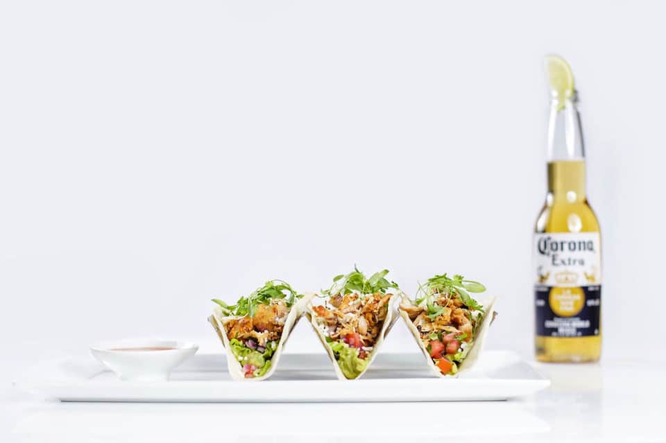 Three fish tacos on white plate with Corona beer and sauce