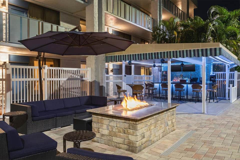 Luxury outdoor patio with firepit, lounge seating, umbrellas, and covered bar area at night