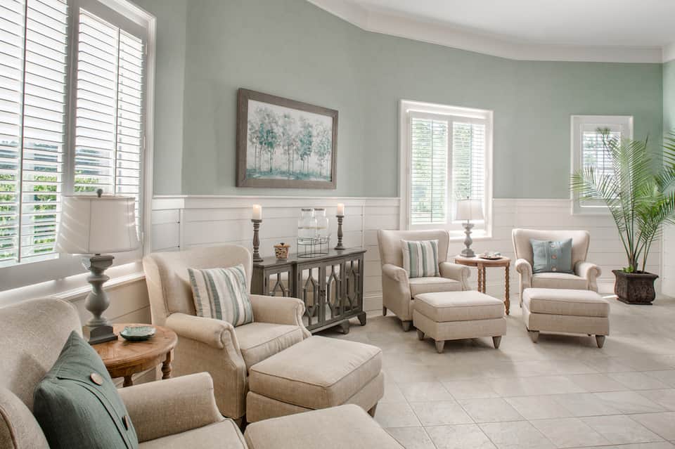 Elegant lounge area with beige armchairs, striped pillows, and coastal decor with shuttered windows