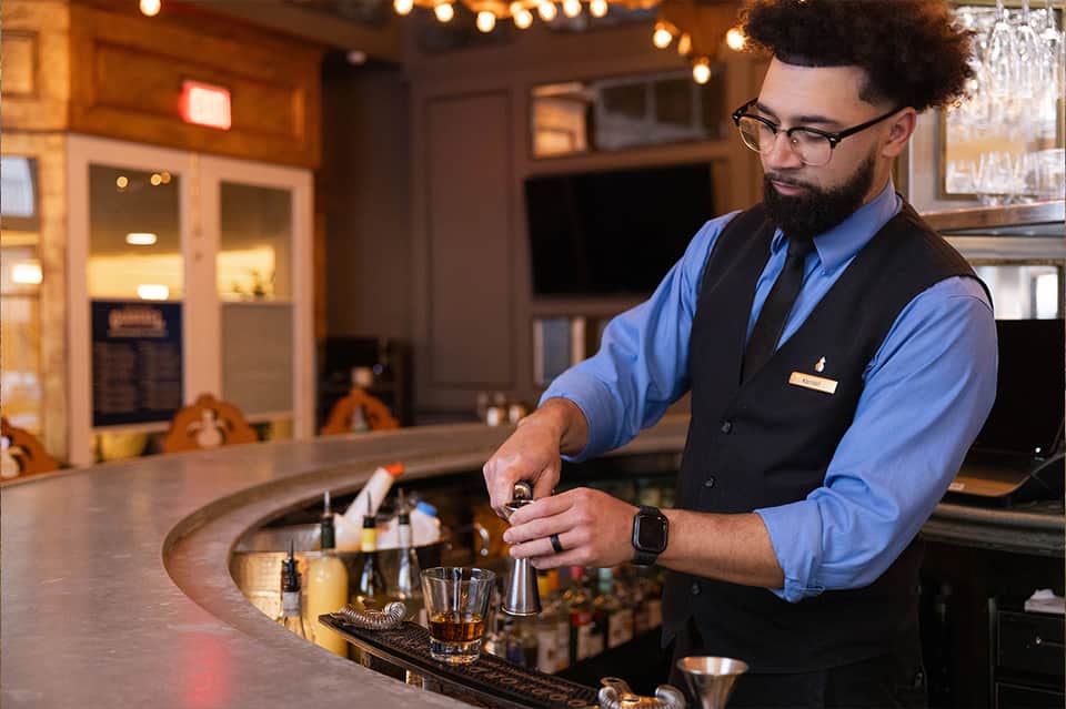 Bartender in vest preparing cocktail at elegant hotel bar with warm lighting