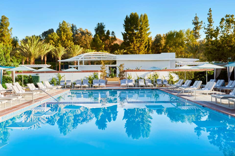 Resort swimming pool with crystal blue water reflecting palm trees and white buildings